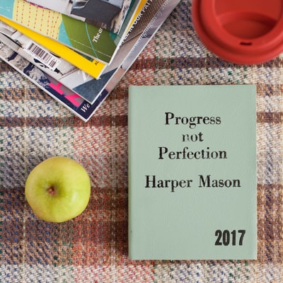 哈珀·梅森（Harper Mason，2017）写的一本书上写着“进步而非完美”，放在苹果和其他书籍旁边。